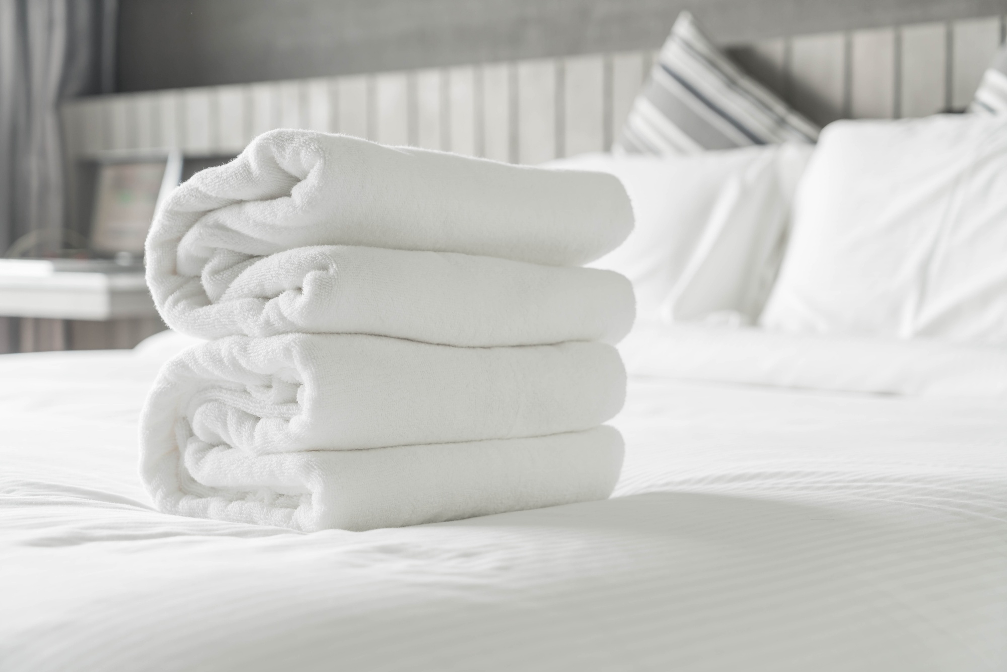 Cama con ropa de cama blanca y toallas blancas dobladas de un sólo color en una vivienda vacacional